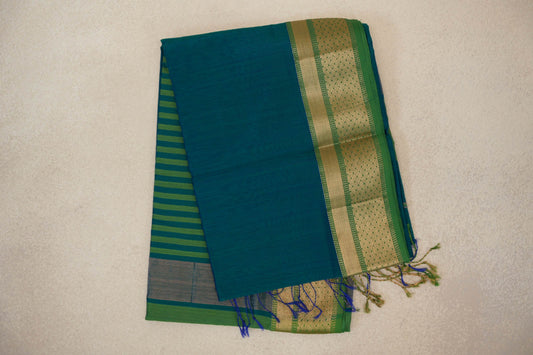 Folded peacock green Maheshwari silk cotton saree with a leaf green and gold-patterned border, striped pallu peeking out and tassels.