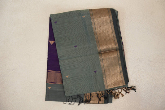 Folded sage green Maheshwari silk cotton saree with small triangle motifs, a wide patterned dark sage green border, and a glimpse of deep purple fabric.