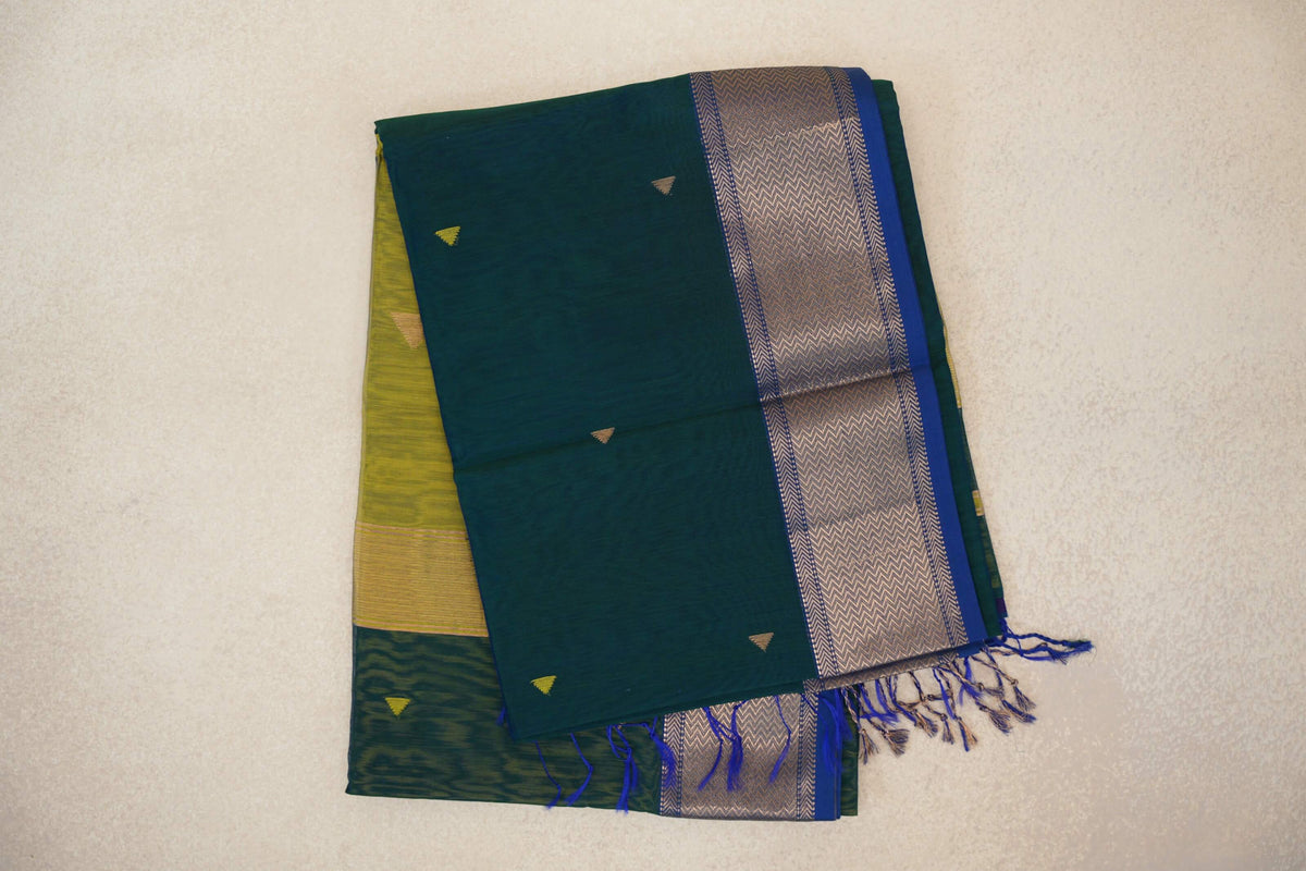 Folded Maheshwari silk cotton saree with a peacock green body, small triangular motifs, a chevron-patterned royal blue border and blue tassels.
