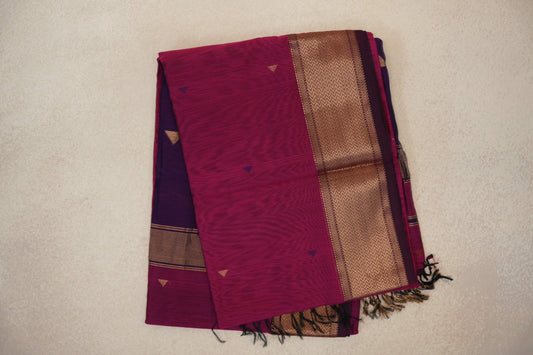 Folded Deep Rani Pink Maheshwari silk cotton saree with small triangular accents, a gold-toned chevron border and a glimpse of the Deep Purple pallu with tassels.