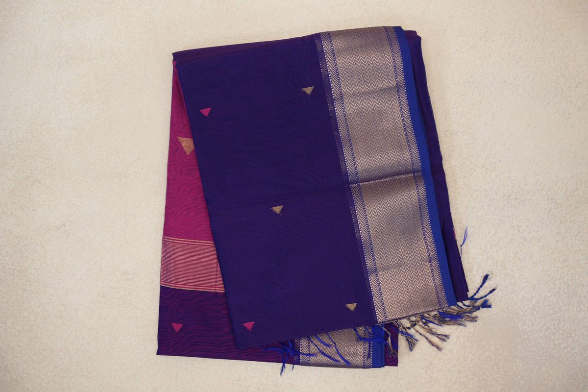 Folded deep violet Maheshwari silk cotton saree with small triangle accents, a metallic chevron border, deep rani pink fabric beneath and tassels.