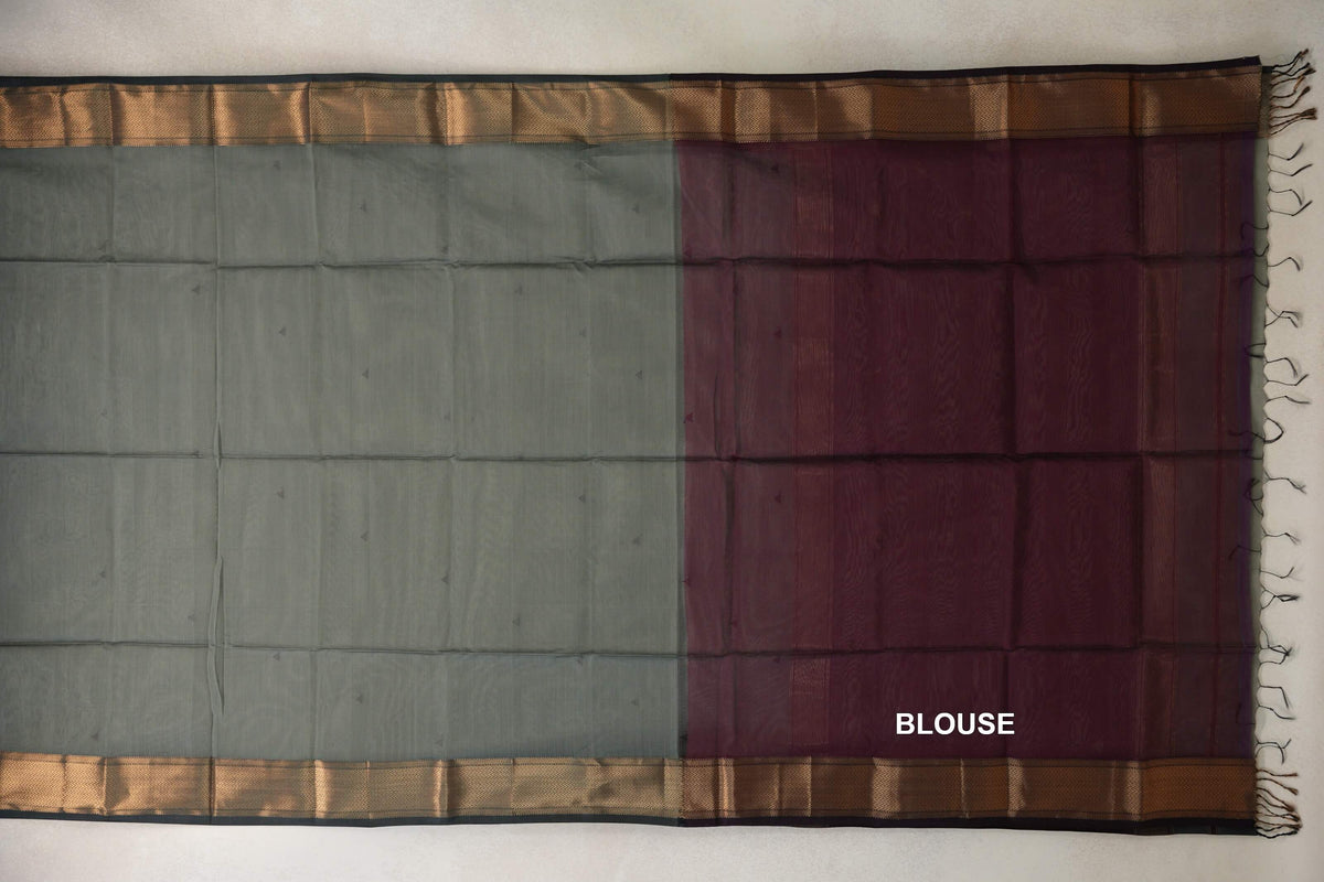 Saree laid flat, showing a sage green silk cotton body with small motifs, gold-toned borders and a deep wine maroon blouse panel.
