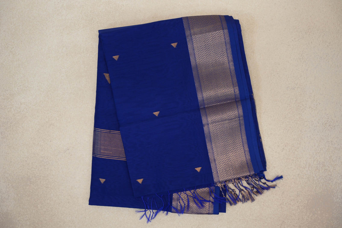 Folded deep royal blue Maheshwari silk cotton saree with small gold-toned triangular motifs, a chevron-patterned border and blue tassels.