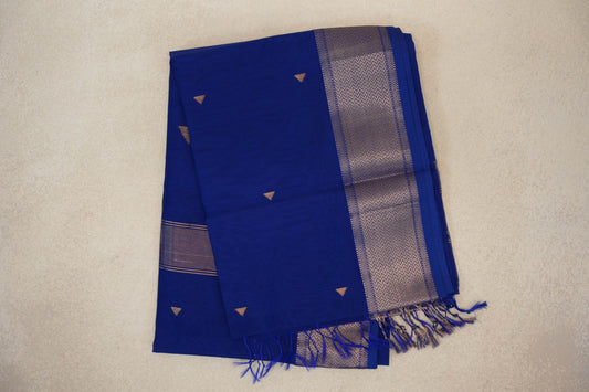 Folded deep royal blue Maheshwari silk cotton saree with small gold-toned triangular motifs, a chevron-patterned border and blue tassels.