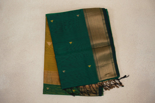 Folded bottle green Maheshwari silk cotton saree with small triangular motifs, a gold-toned zigzag border, mustard yellow fabric and tassels.