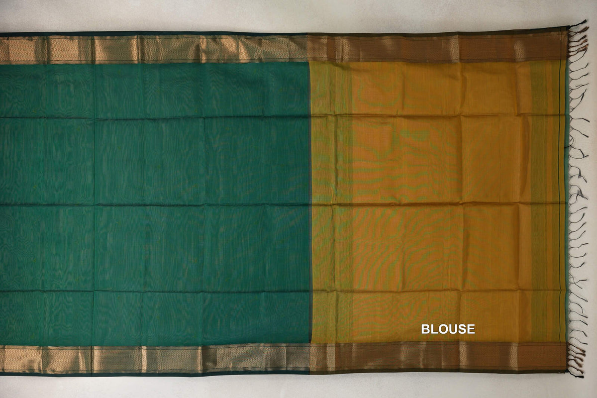 Bottle green Maheshwari silk cotton saree laid flat beside its mustard yellow blouse fabric, with patterned borders and tassels at the right edge.