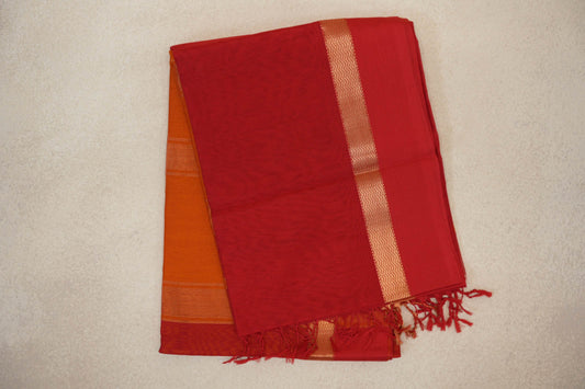 Folded vermilion red Maheshwari silk-cotton saree with a gold-toned zigzag border, deep orange fabric peeking beneath and red tassels.