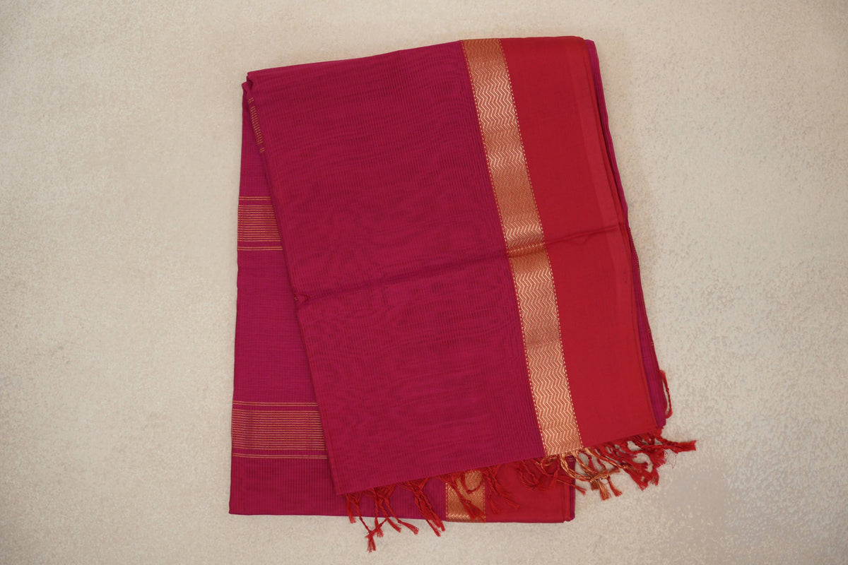 Folded bright rani pink Maheshwari silk cotton saree with a deep rani pink border, gold zigzag band, fine stripes and tassels.