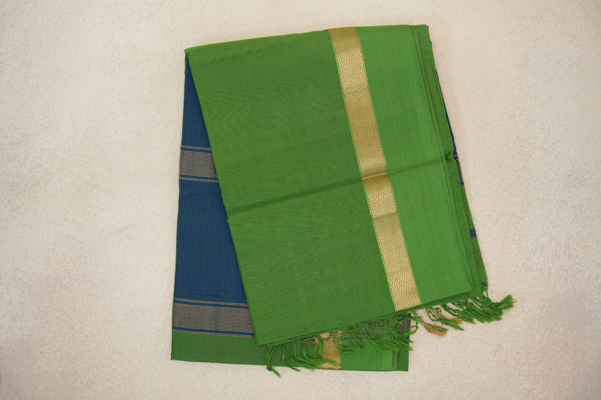 Folded bright leaf green Maheshwari silk cotton saree with a gold zigzag stripe, peacock blue section peeking out beneath, and green tassels.
