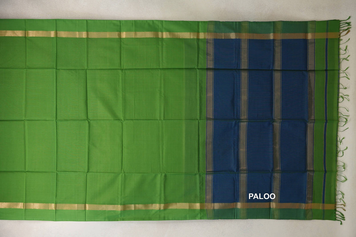 Maheshwari silk cotton saree laid flat, with a bright leaf green body, gold-toned borders and a striped peacock blue pallu with tassels.