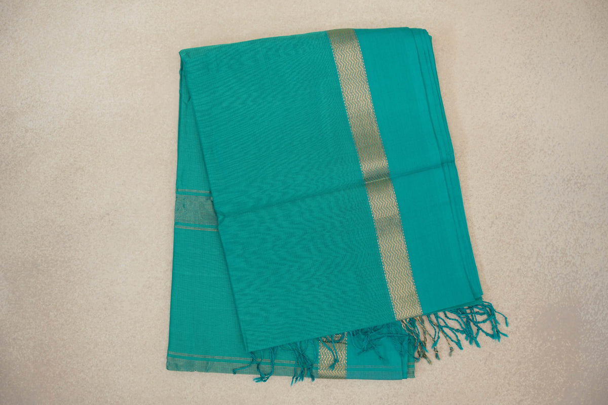 Folded bright aqua green Maheshwari silk-cotton saree with a narrow gold zigzag border, fine striped edging and tassels.