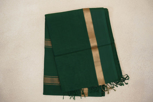Folded deep bottle green Maheshwari silk cotton saree with fine vertical texture, a gold-toned border, narrow stripes and tassels.