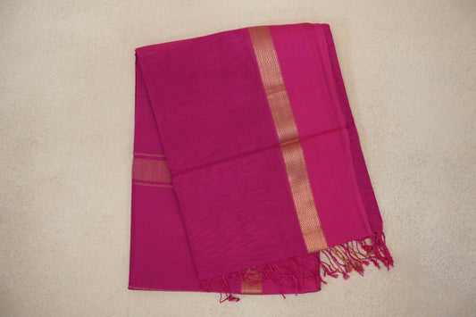 Folded bright rani pink Maheshwari silk cotton saree with a fine checked texture, gold-tone zigzag border and pink tassels.