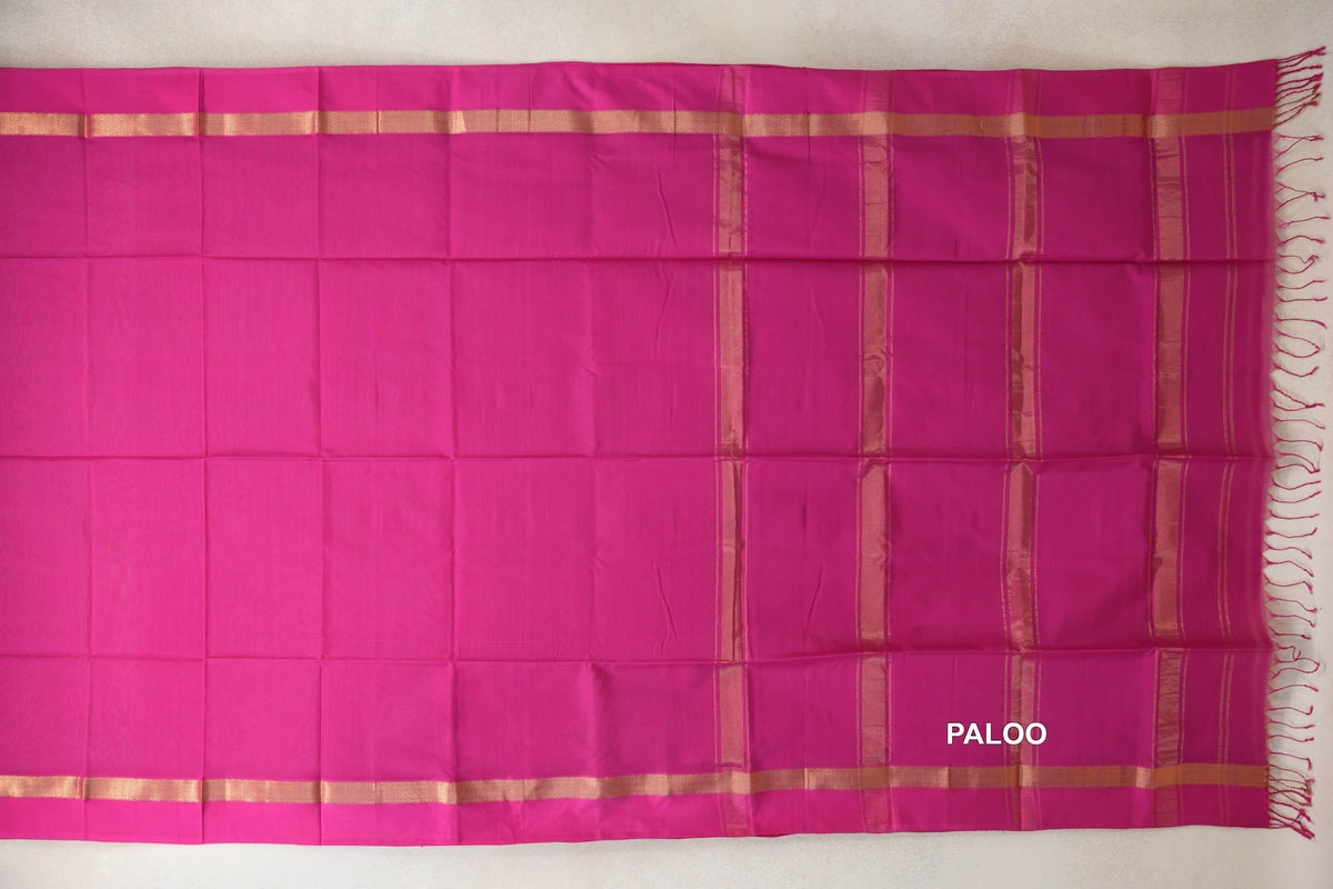 Bright rani pink Maheshwari silk cotton saree spread flat, with gold-toned borders and a striped pallu ending in pink tassels.