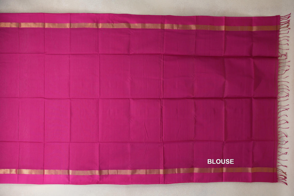 Bright rani pink silk cotton saree blouse section laid flat, with narrow gold-toned borders along the top and bottom and pink tassels at one end.