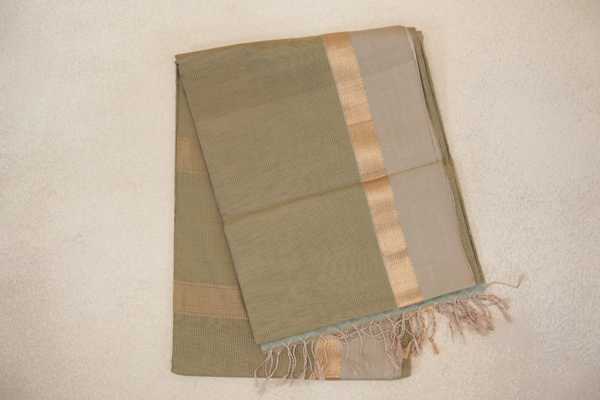 Folded light olive green Maheshwari silk cotton saree with fine stripes, a light beige border, gold zigzag detailing and tassels.