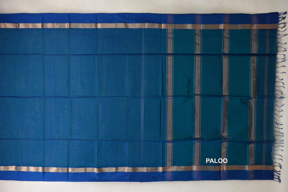 Peacock Blue Maheshwari silk cotton saree laid flat, with Deep Peacock Blue borders, silver-toned bands and a striped pallu with tassels.