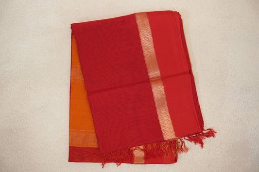 Folded red Maheshwari silk cotton saree with fine stripes, a gold-toned zigzag border, red tassels and orange fabric peeking beneath.