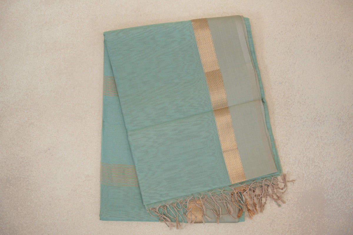 Folded sea green Maheshwari silk cotton saree with a fine checked body, light sandal beige border, gold zigzag band and tasselled edge.