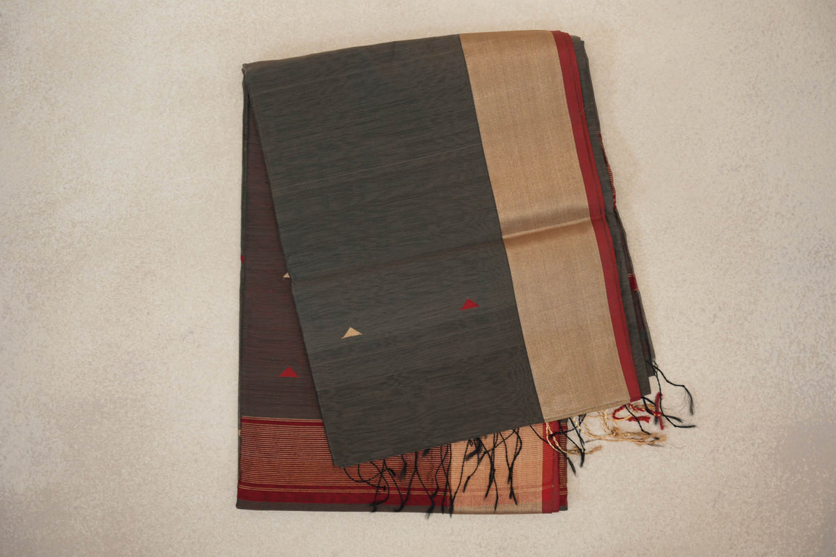 Folded charcoal grey Maheshwari silk-cotton saree with small red and gold triangles, a broad gold-toned band, deep red edge and loose tassels.