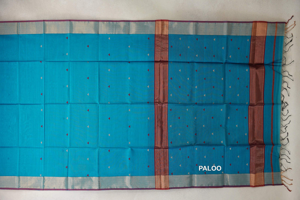 Maheshwari silk cotton saree laid flat, showing a bright turquoise blue pallu with tiny triangular motifs, deep red bands, pale borders and tassels.