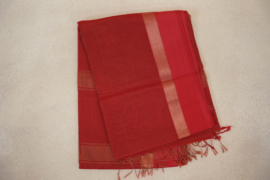 Folded tomato red Maheshwari silk cotton saree with fine pinstripes, a narrow zigzag band, a plain red panel and tassels along the edge.