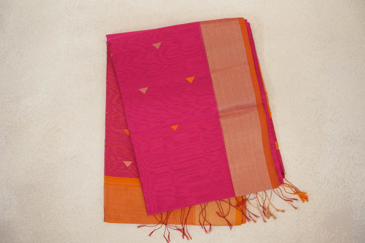 Folded rani pink Maheshwari silk cotton saree with small triangular motifs, a broad orange border and loose tassels at one end.