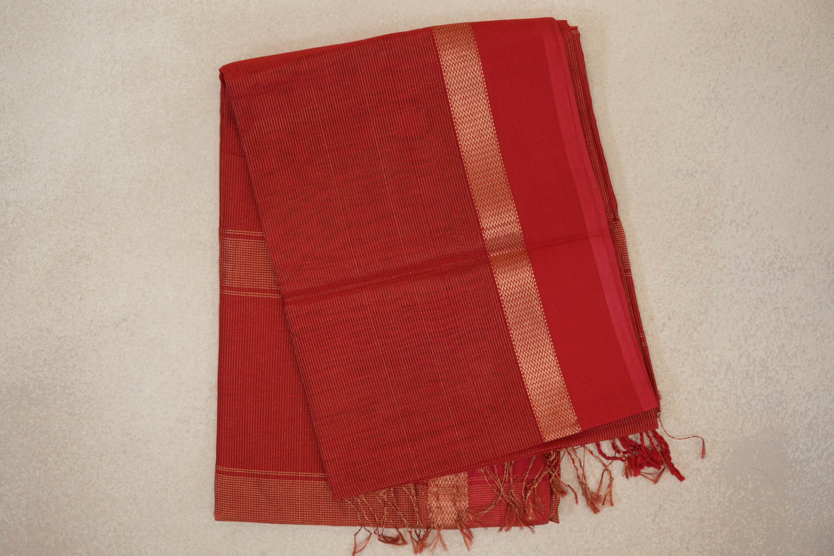 Folded red Maheshwari silk-cotton saree with fine pinstripes, a chevron-patterned band beside a plain red border, and tassels at the end.