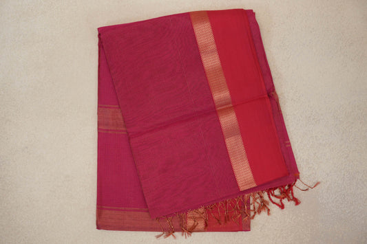 Folded Rani Pink Maheshwari silk cotton saree with fine stripes, a plain panel beside a patterned border, and tassels at the end.
