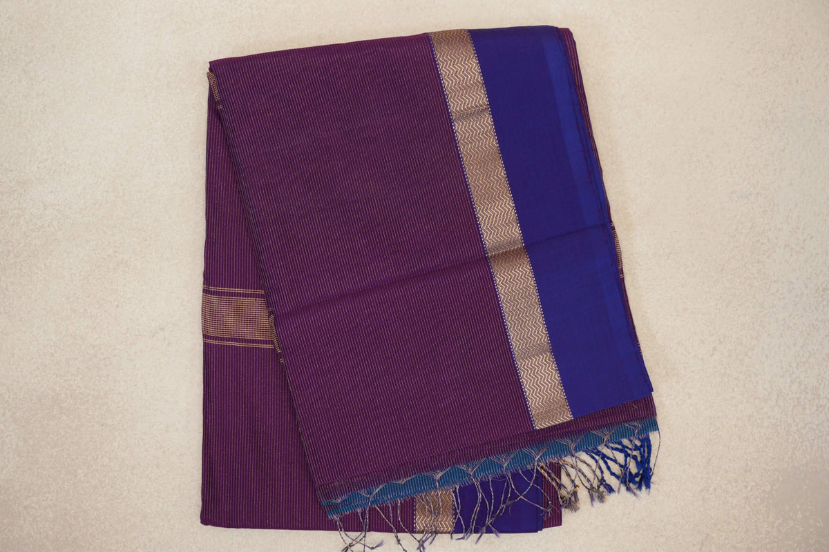 Folded Maheshwari silk cotton saree with a finely striped deep purple body, violet purple border, gold zigzag band and tasseled end.