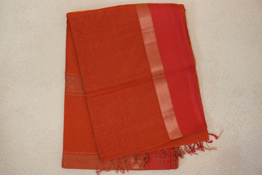 Folded rust orange Maheshwari silk cotton saree with fine stripes, a red border edged in a pale zigzag pattern, and tassels at one end.
