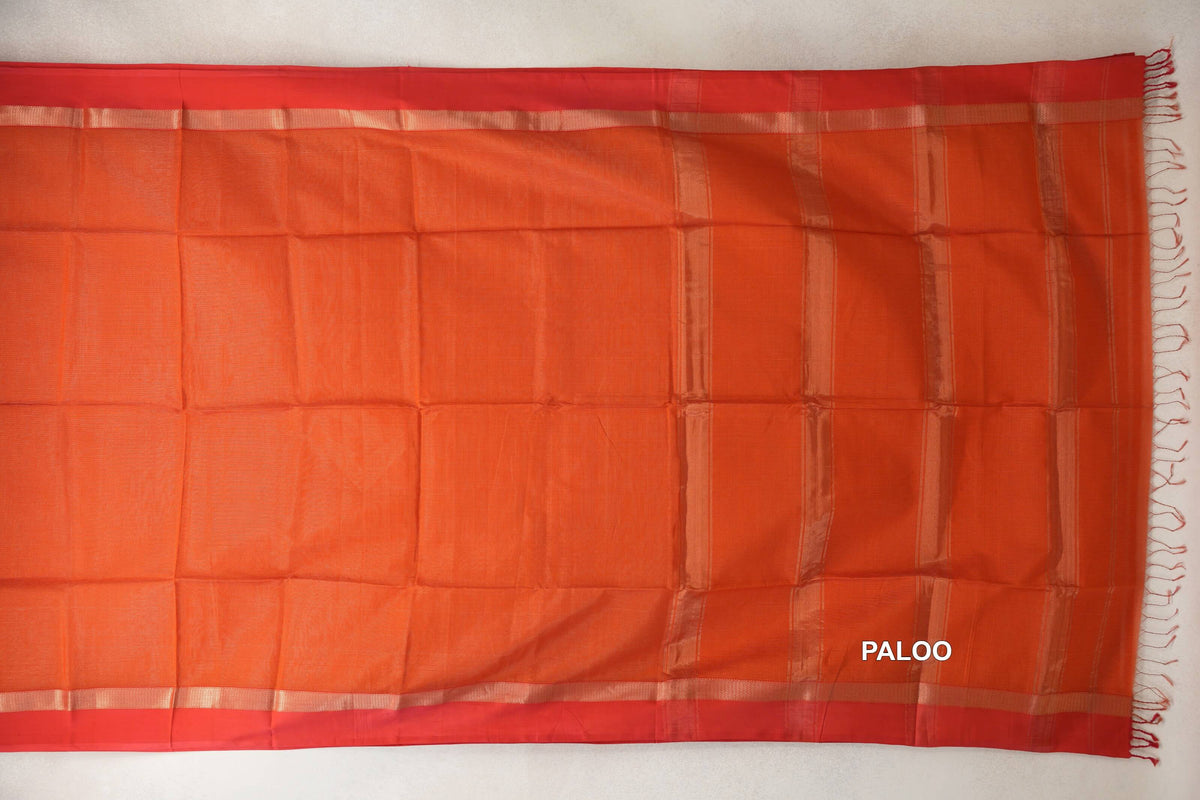 Rust orange Maheshwari silk cotton saree laid flat, with red borders, shimmering stripes on the pallu at right, and tassels along the end.