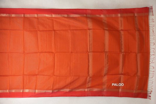 Rust orange Maheshwari silk cotton saree laid flat, with red borders, shimmering stripes on the pallu at right, and tassels along the end.