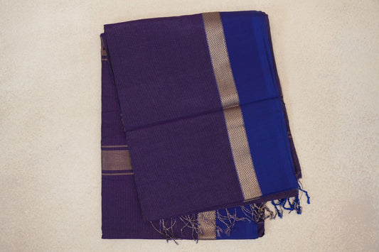 Folded deep purple Maheshwari silk cotton saree with fine stripes, a violet border, gold-toned zigzag detailing and a fringed edge.