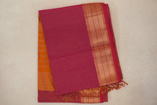 Folded rani pink Maheshwari silk cotton saree with fine stripes, a gold-toned patterned border, orange fabric peeking out and tassels.