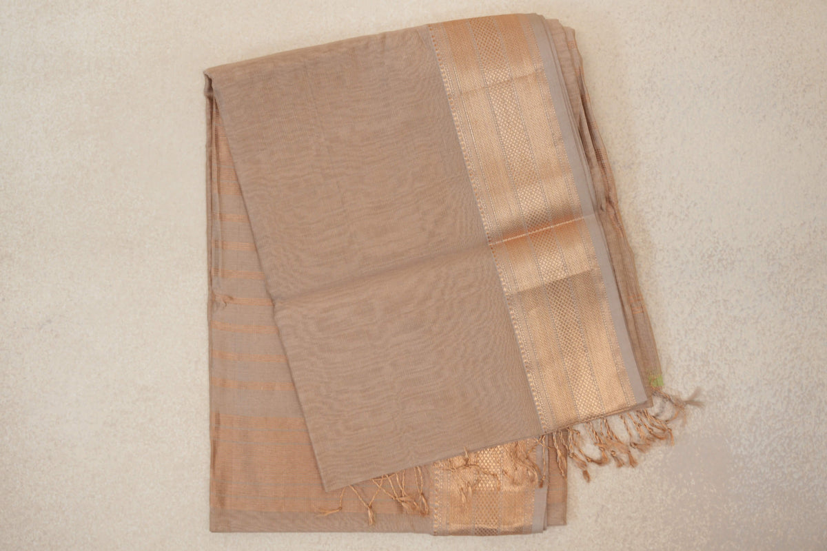 Folded Dark Sandal Beige Maheshwari silk cotton saree with a plain body, lustrous patterned border, fine stripes and tasselled edge.