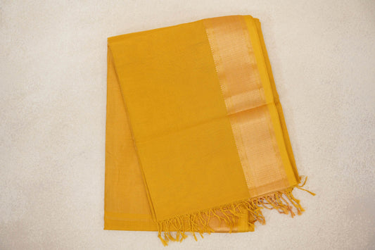 Folded mustard yellow Maheshwari silk cotton saree with a fine checked texture, a shimmering woven border and tassels along the edge.