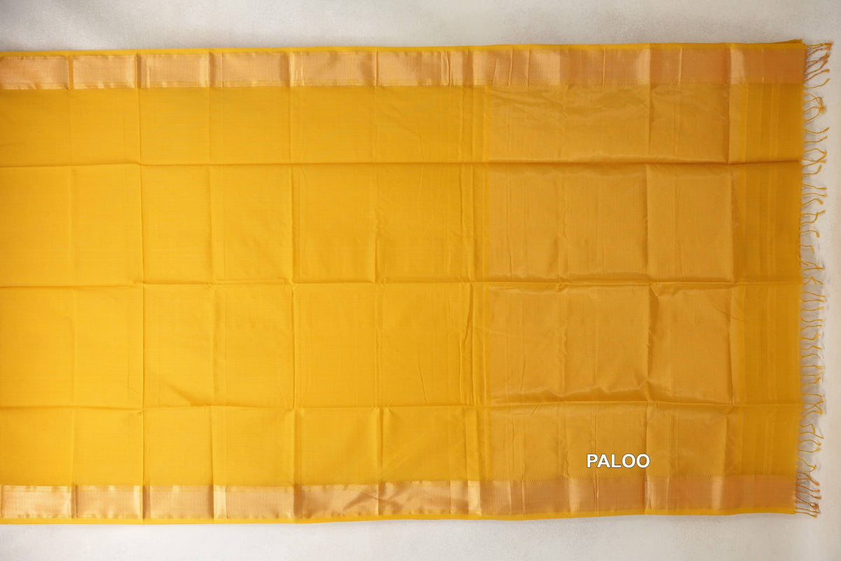 Mustard yellow Maheshwari silk cotton saree laid flat, showing a plain body, lustrous borders and a tonal pallu with tassels at the right edge.