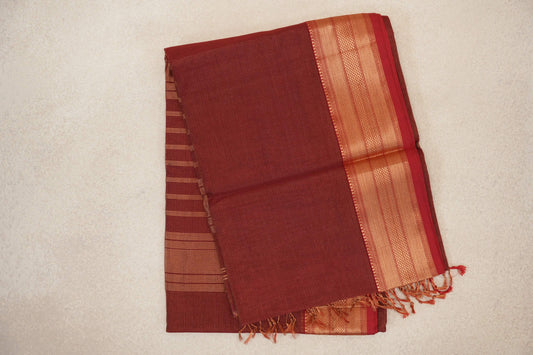 Folded brick red Maheshwari silk cotton saree with fine pinstripes, a patterned gold-toned border and tassels.