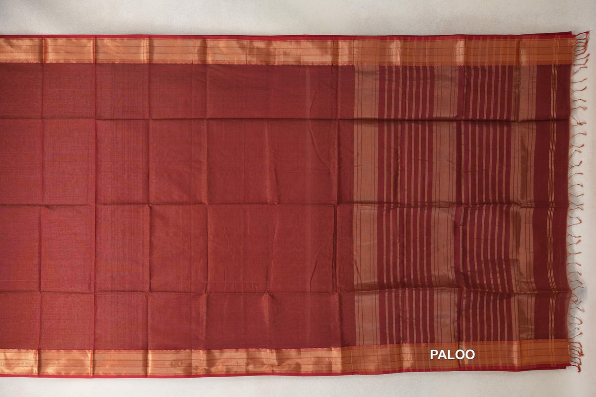 Brick red Maheshwari silk cotton saree spread flat, with a plain body, copper-toned borders and a striped pallu with tassels.