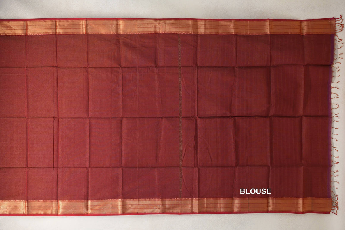 Brick red Maheshwari silk cotton blouse fabric laid flat, with gold-toned striped borders and tassels along one edge.