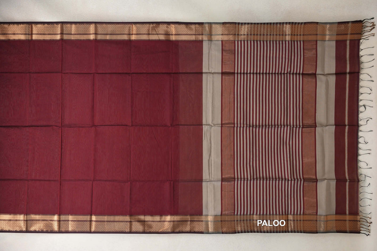 Maroon Maheshwari silk cotton saree laid flat, with patterned borders and a grey-and-maroon striped pallu ending in tassels.