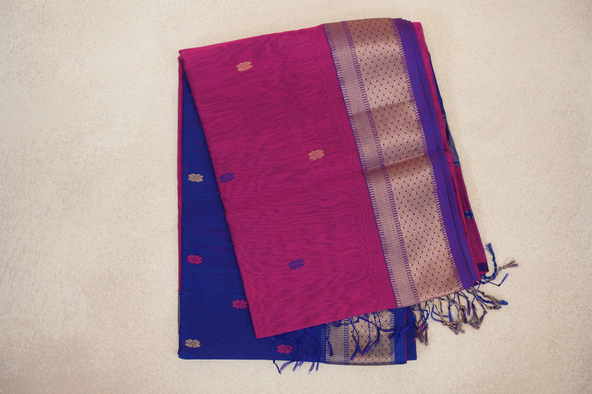 Folded Maheshwari silk cotton saree with a bright rani pink body, small floral motifs, a gold-patterned royal purple border and a royal blue layer with tassels.