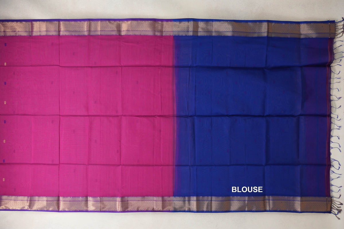 Maheshwari silk cotton saree laid flat, showing a bright rani pink body, royal blue blouse section, patterned royal purple borders and blue tassels.
