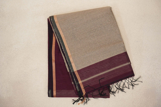 Folded wine maroon Maheshwari silk cotton saree with a sand beige striped pallu, maroon end band and dark tassels.