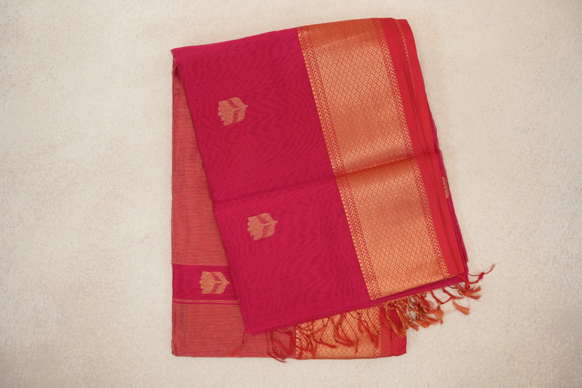 Folded Deep Rani Pink Maheshwari silk cotton saree with small gold motifs, a patterned Pinkish Red border, striped fabric and tassels.