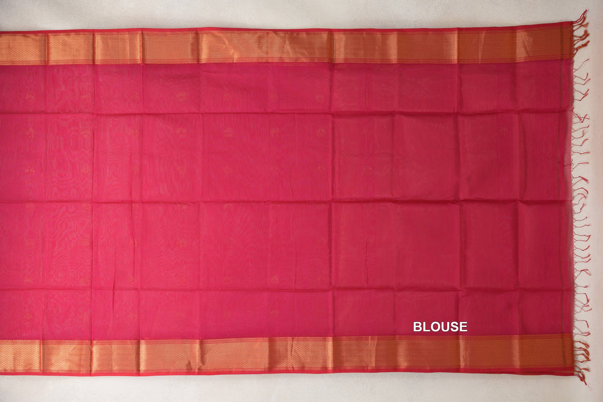 Deep Rani Pink Maheshwari silk cotton blouse fabric laid flat, with broad gold-toned borders, Pinkish Red selvedge and tassels along one edge.