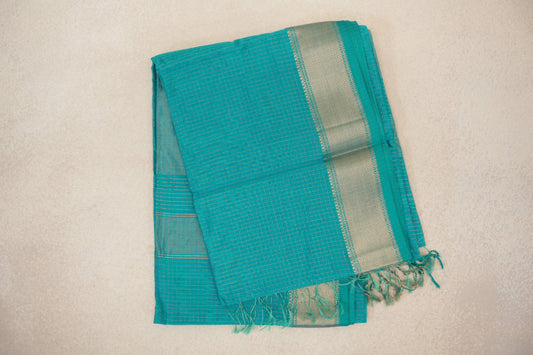 Folded turquoise green Maheshwari silk-cotton saree with fine checks, a shimmering woven border and tassels at the pallu end.