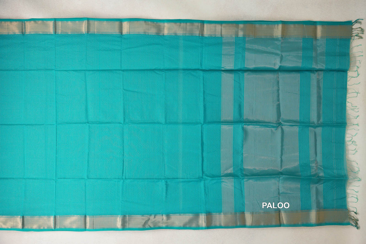 Turquoise green Maheshwari silk-cotton saree spread flat, showing a fine checked body, pale metallic borders and a striped pallu with tassels.