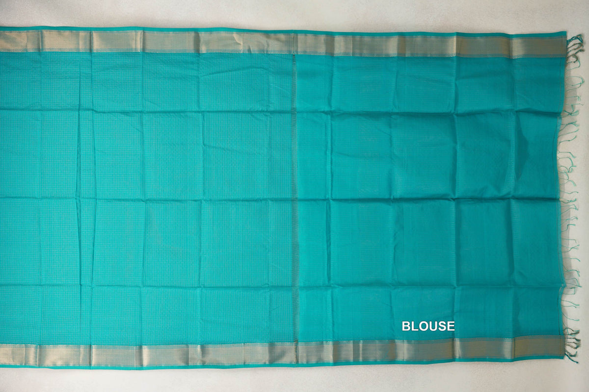 Turquoise green Maheshwari silk-cotton saree laid flat, showing a finely checked body, pale shimmering borders and a plain blouse section with tassels.